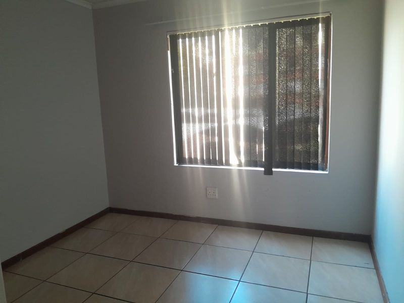 A bright, empty bedroom featuring neutral tiled flooring and vertical window blinds, providing a clean and versatile space ready for personalization.