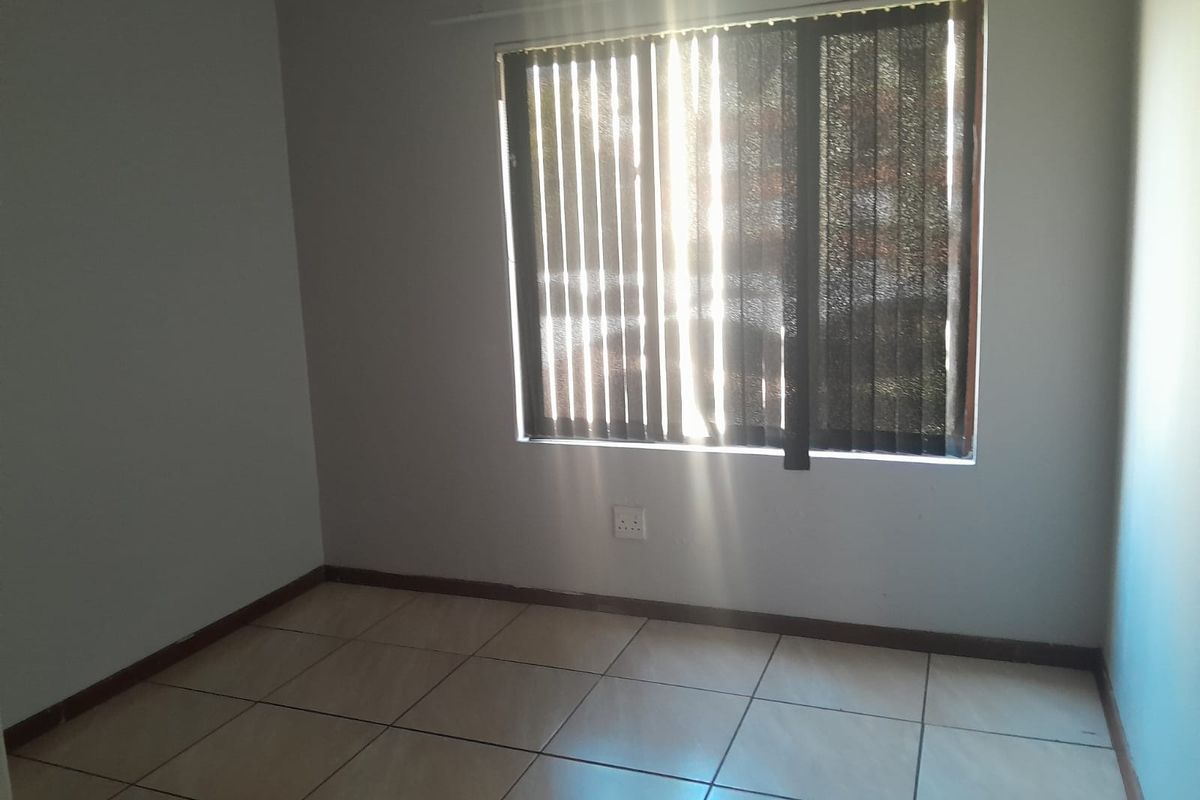 A bright, empty bedroom featuring neutral tiled flooring and vertical window blinds, providing a clean and versatile space ready for personalization.