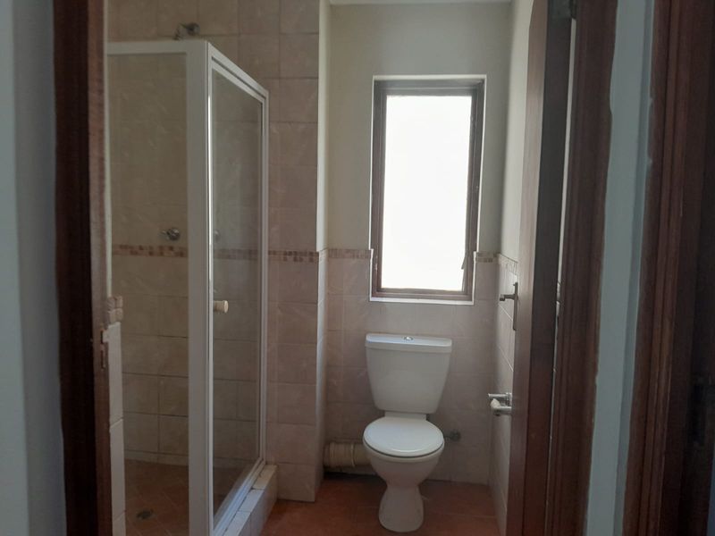 A functional bathroom featuring a shower enclosure, toilet, and tiled finishes, offering a clean and simple layout ready for potential cosmetic updates.