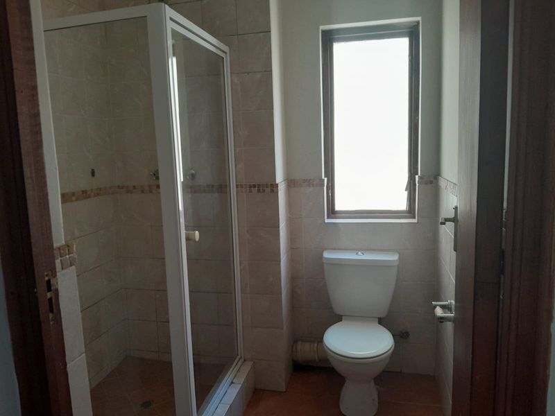 A functional bathroom featuring a shower enclosure, toilet, and neutral wall and floor tiling, offering a clean and practical layout.