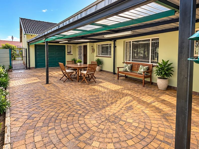 A well-maintained covered patio area featuring decorative circular paving, a metal roof structure, and direct access to the garage and garden.