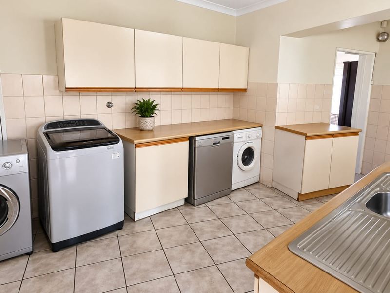 Functional laundry room featuring ample built-in cabinetry, laminate countertops, tiled splashbacks, and a stainless steel sink with tiled flooring.