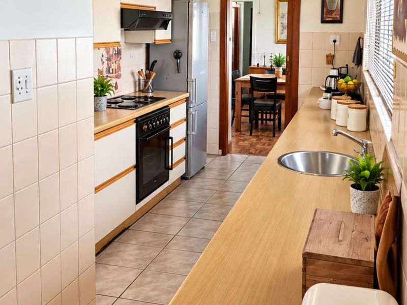 A functional galley-style kitchen featuring light-toned cabinetry, laminate countertops, a built-in oven with hob, and tiled flooring throughout.