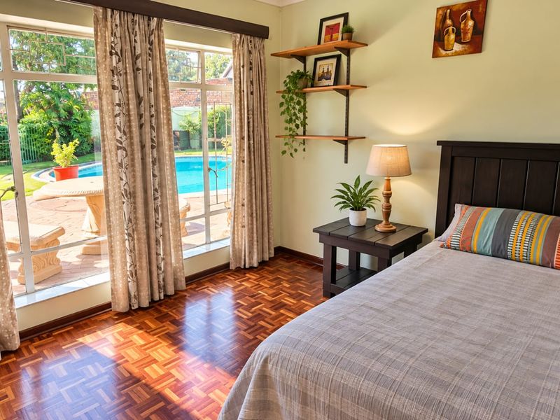 A well-maintained bedroom featuring warm parquet flooring and a large glass sliding door that provides direct access to the outdoor pool area.