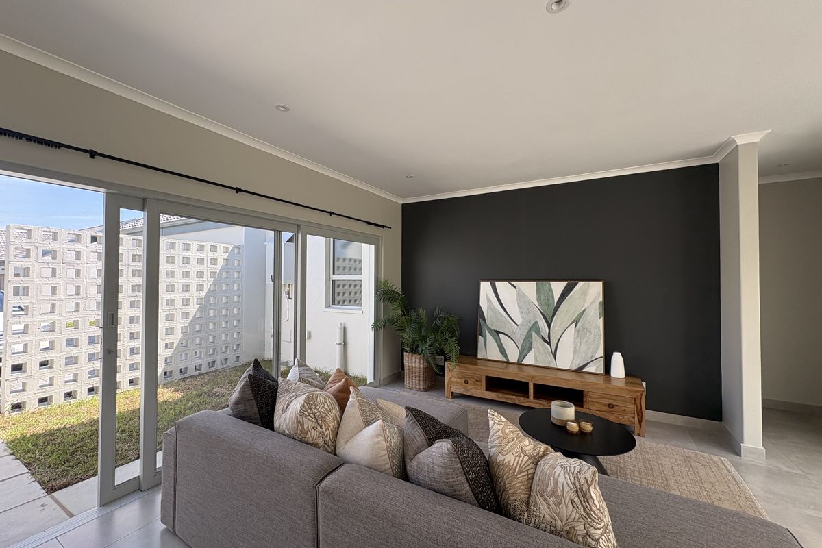 A bright living room featuring large sliding glass doors that open to an outdoor area, complemented by modern tiled flooring and a feature wall.