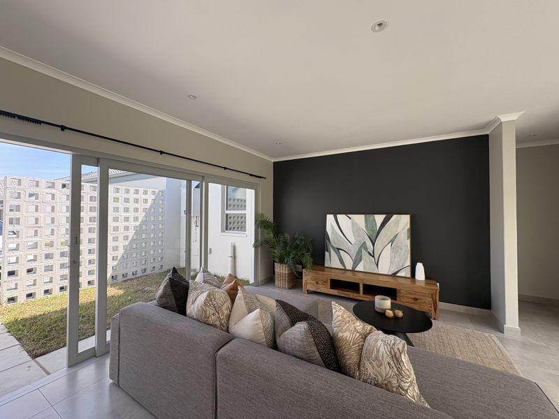 A bright living room featuring large sliding glass doors that open to an outdoor area, complemented by modern tiled flooring and a feature wall.