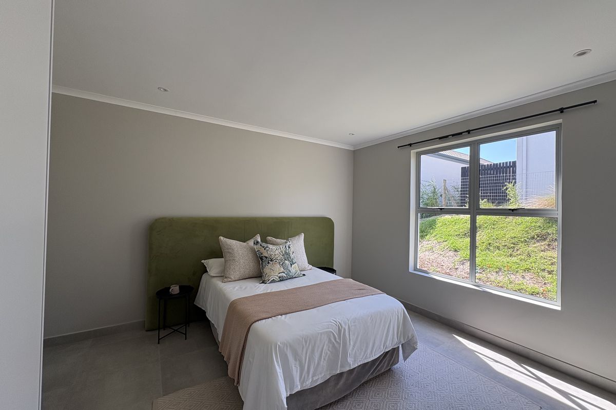 A bright and modern bedroom featuring neutral wall tones, tiled flooring, recessed downlights, and a large window providing natural light and garden views.