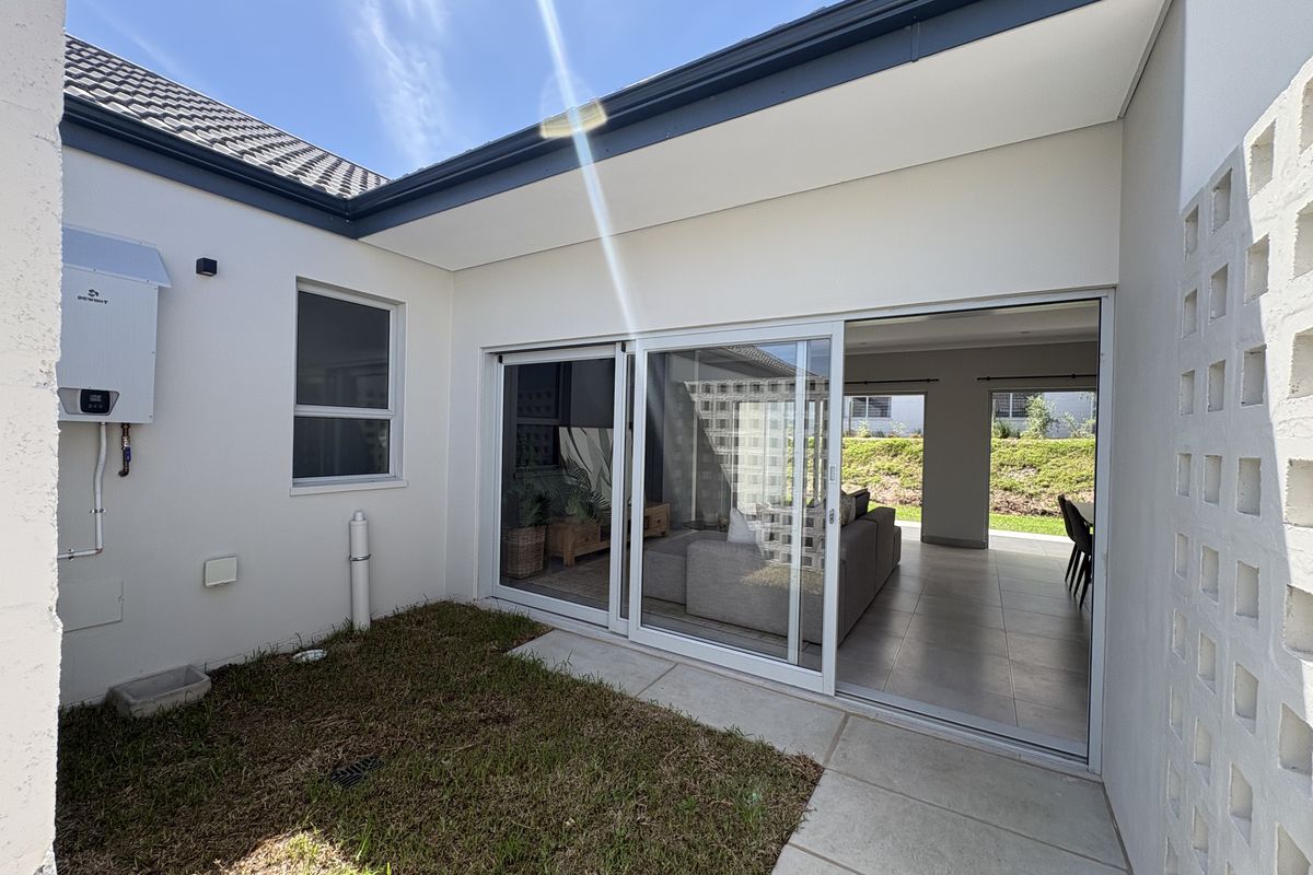 A rear exterior view featuring a paved patio area, sliding glass doors leading into the living space, and a wall-mounted gas water heater.