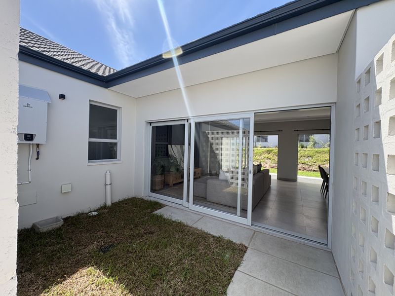 A rear exterior view featuring a paved patio area, sliding glass doors leading into the living space, and a wall-mounted gas water heater.