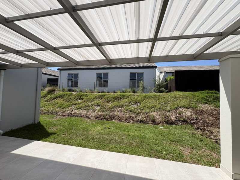 A covered patio area featuring a translucent roof and tiled flooring, overlooking a private garden and neighbouring residential properties.
