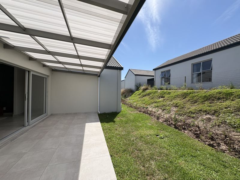 A clean, covered patio area with tiled flooring and sliding glass doors, overlooking a landscaped garden and neighbouring cluster homes.