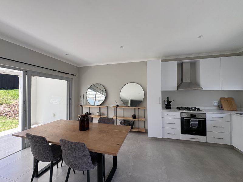 Modern open-plan kitchen and dining area featuring sleek white cabinetry, integrated appliances, tiled floors, and large sliding doors leading to the outdoor patio.