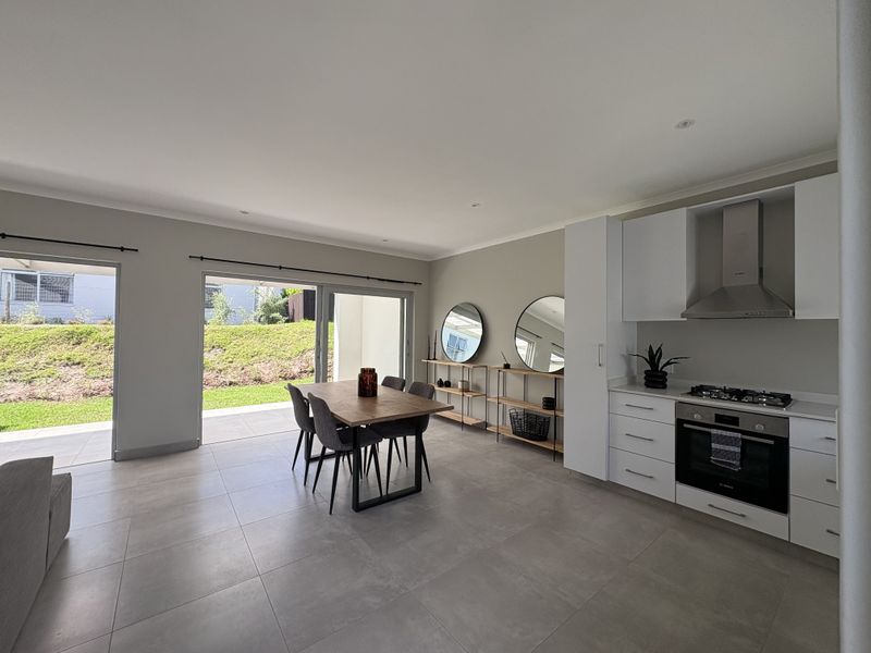 Modern open-plan living and kitchen area featuring sleek white cabinetry, integrated appliances, large format floor tiles, and seamless access to the outdoor patio.