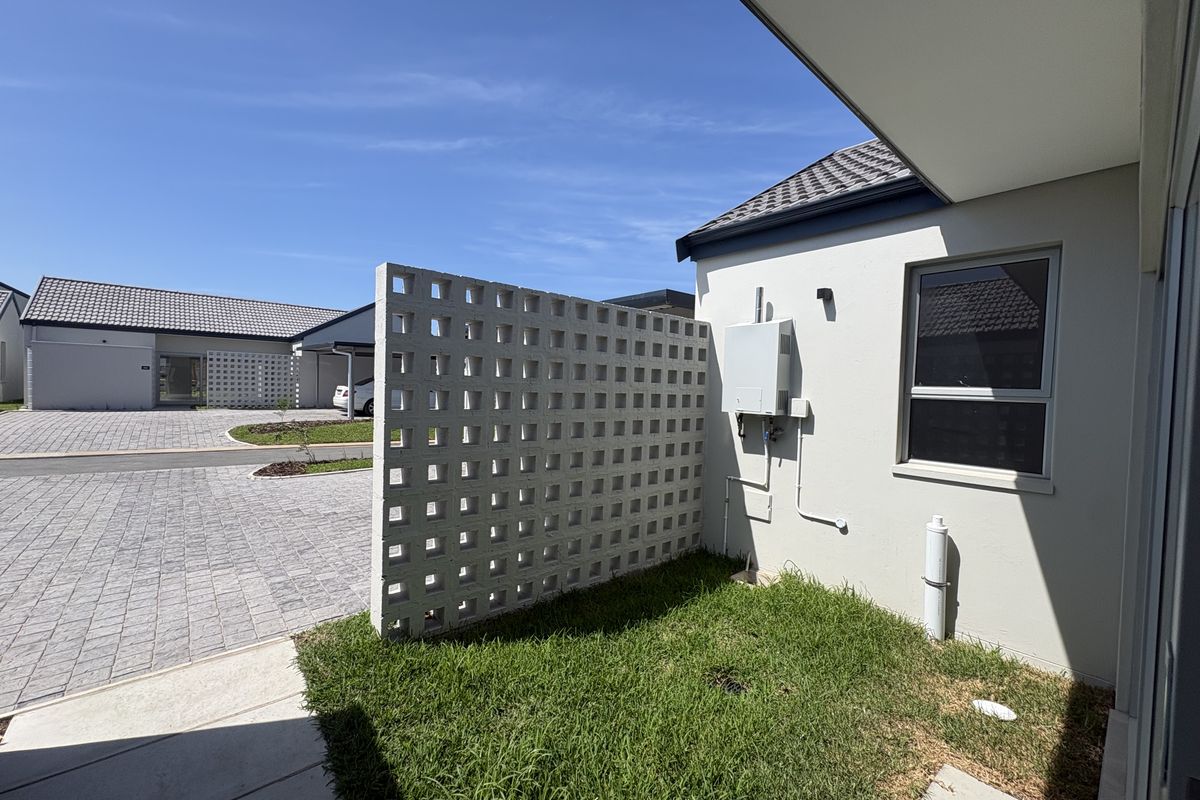 A private rear garden area featuring a decorative breeze block privacy screen, paved driveway access, and well-maintained exterior wall finishes.
