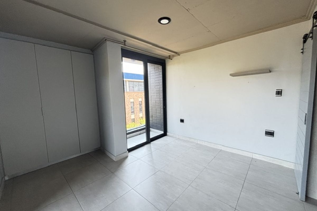 A bright, modern bedroom featuring built-in cupboards, tiled flooring, and a sliding glass door leading to an outdoor area.