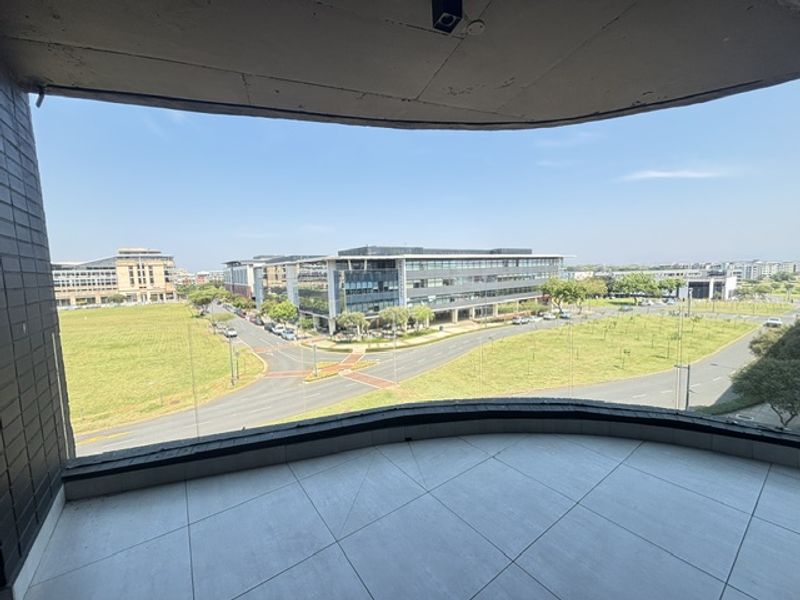 A spacious balcony featuring modern tiled flooring and a clear glass balustrade, offering an expansive view of the surrounding urban landscape.