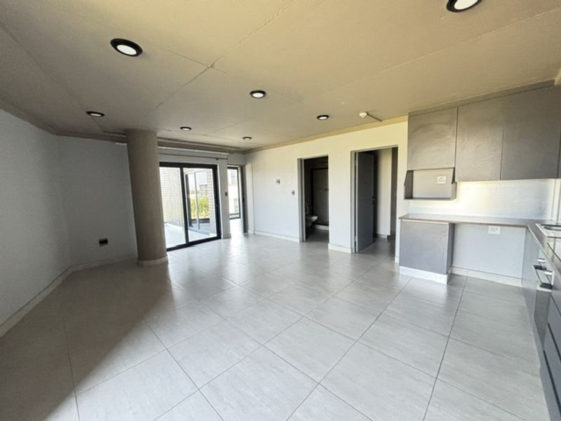 Spacious open-plan living and kitchen area featuring modern grey cabinetry, neutral tiled flooring, recessed lighting, and direct access to an outdoor balcony.