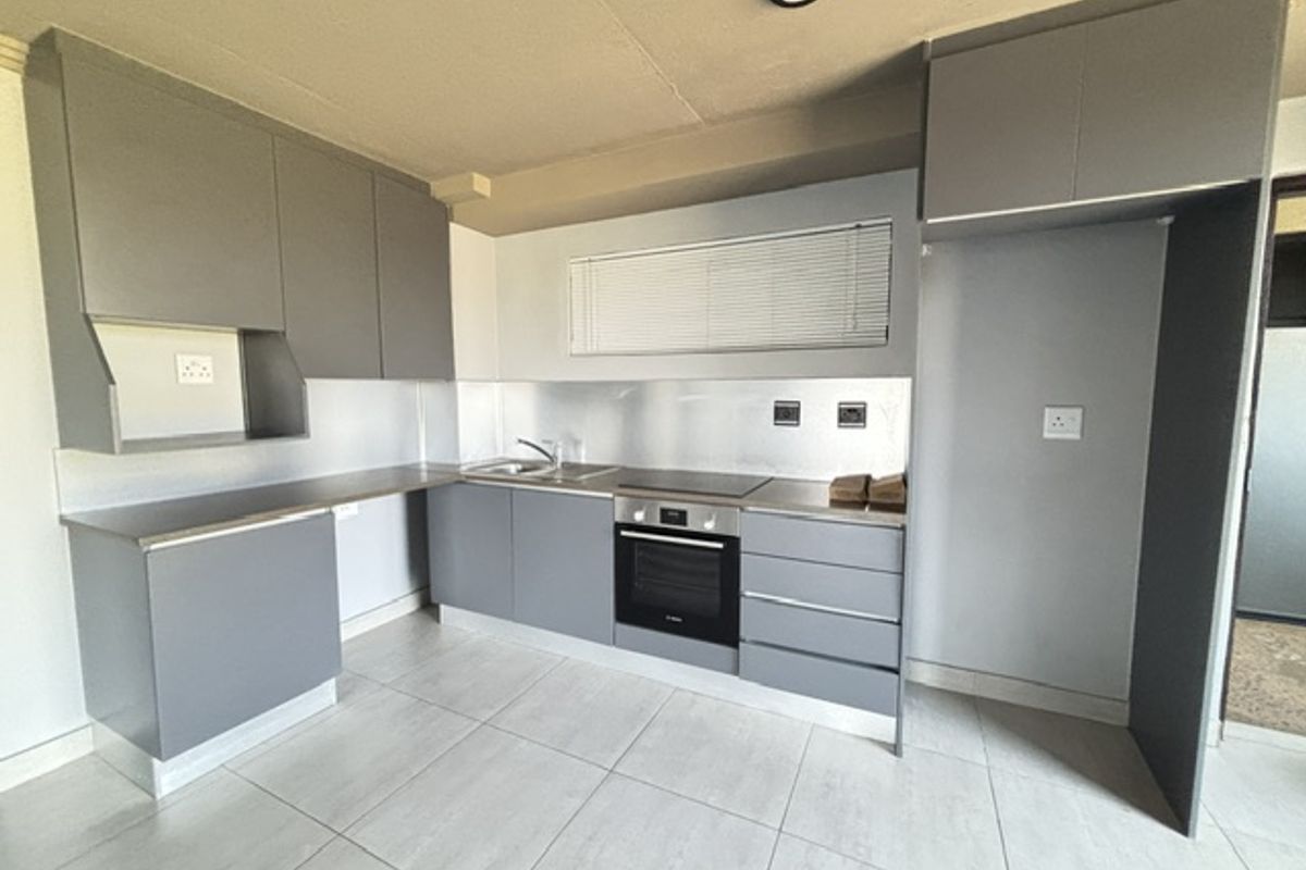 Modern kitchen featuring sleek grey cabinetry, stainless steel splashback, integrated oven and hob, and tiled flooring in a clean, minimalist layout.