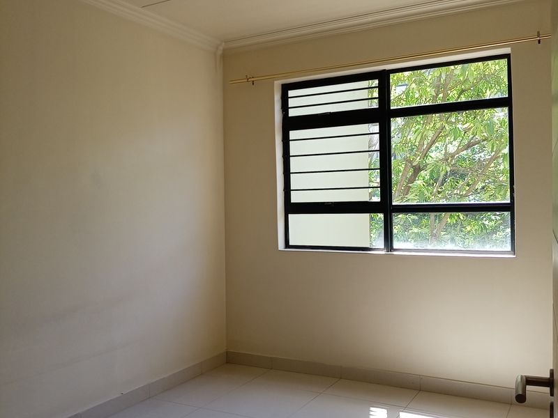 A bright, empty bedroom featuring neutral tiled flooring, clean walls, and a window fitted with security bars and a curtain rod.