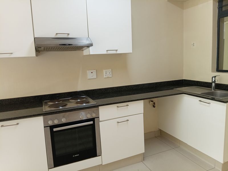 A clean, modern kitchen featuring white cabinetry, granite countertops, a built-in oven, electric hob, and a stainless steel sink.