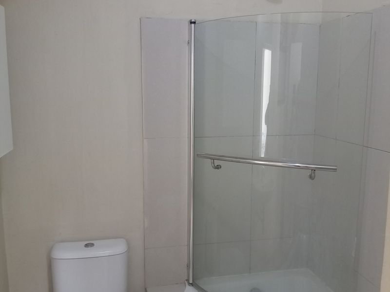 A functional bathroom featuring a curved glass shower enclosure, built-in shower base, and a standard toilet with neutral wall tiling.