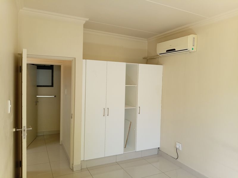 A clean, empty bedroom featuring tiled flooring, a built-in wardrobe, and a wall-mounted air conditioning unit.