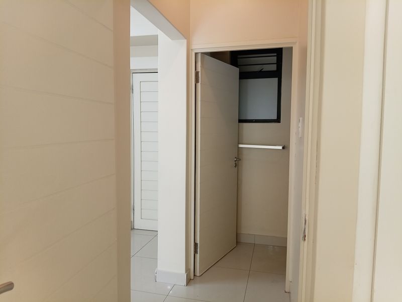A clean, neutral-toned hallway featuring tiled flooring and internal doors leading to adjacent rooms, including a small utility or bathroom space.