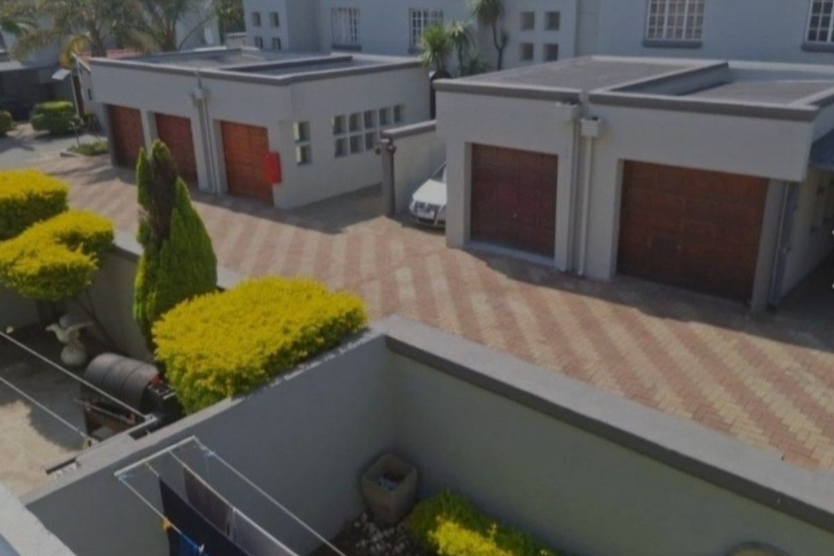 Aerial view of the apartment complex featuring a paved driveway, multiple garages with wooden doors, and well-maintained boundary walls and garden areas.