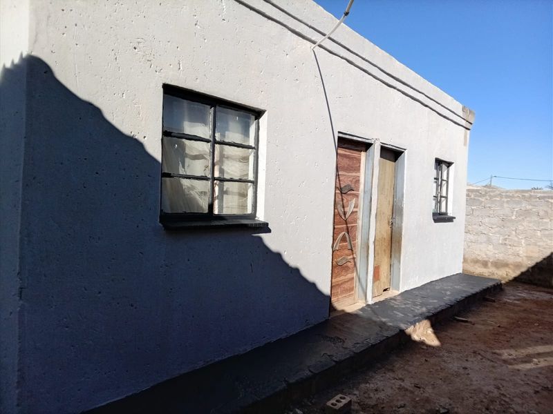 Rear exterior view of the property featuring a concrete apron, metal-framed windows, and two exterior access doors.