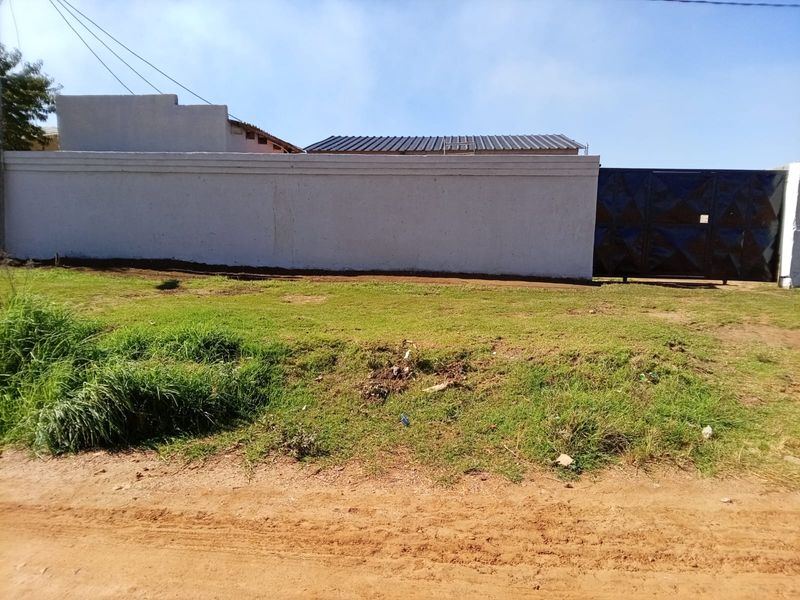 Front view of the property featuring a perimeter wall, metal gate, and corrugated roof structure with an unpaved verge area.