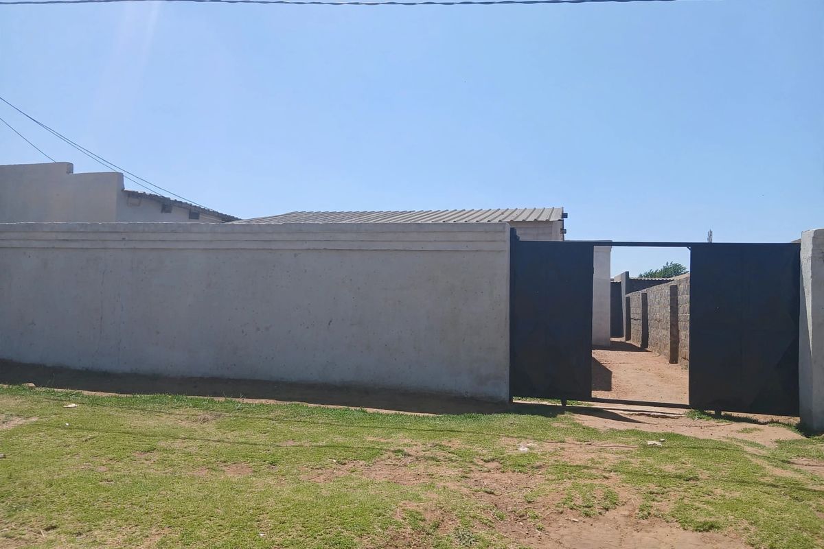 Front view of the property featuring a perimeter wall and metal entrance gate with a corrugated metal roof visible in the background.
