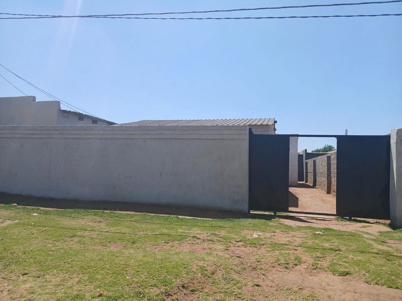 Front view of the property featuring a perimeter wall and metal entrance gate with a corrugated metal roof visible in the background.