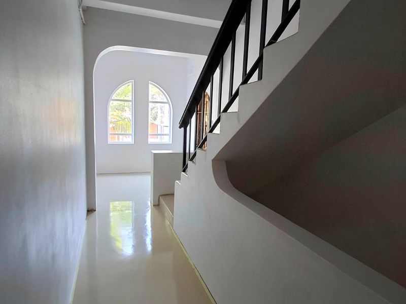 A bright, minimalist hallway featuring a staircase with a metal balustrade and elegant arched windows, finished with clean, reflective tiled flooring.