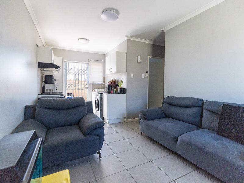 Open-plan living area featuring tiled flooring and a compact kitchen with built-in cabinetry, extractor fan, and direct access to an outdoor area.