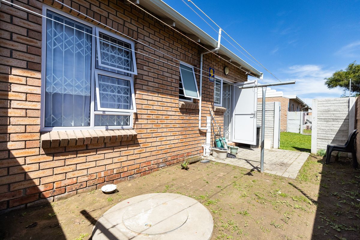 Rear exterior view of the townhouse featuring a brick facade, security-fitted windows, a small paved patio area, and a functional washing line.