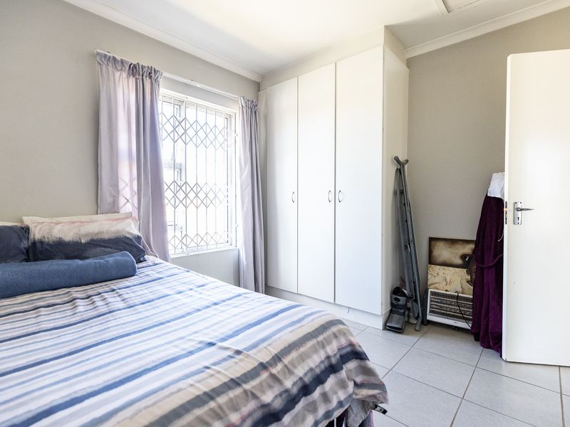 A functional bedroom featuring tiled flooring, a built-in wardrobe, and a window fitted with a security gate.