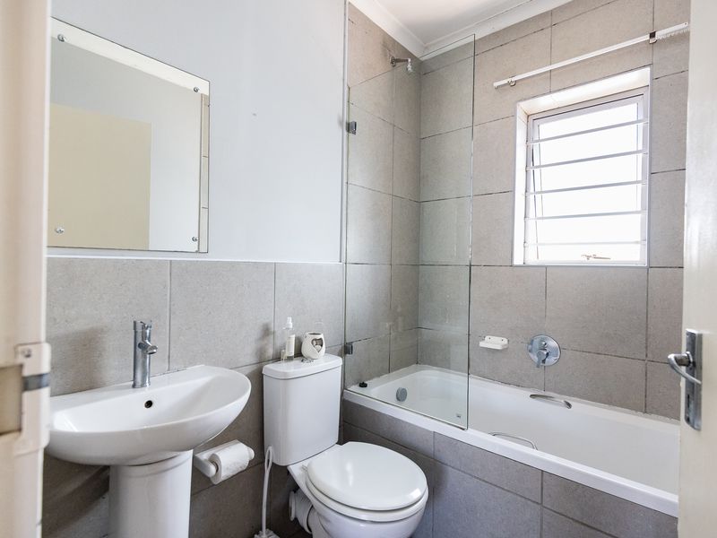 A functional bathroom featuring a pedestal basin, toilet, and a bathtub with a glass shower screen and tiled wall finishes.