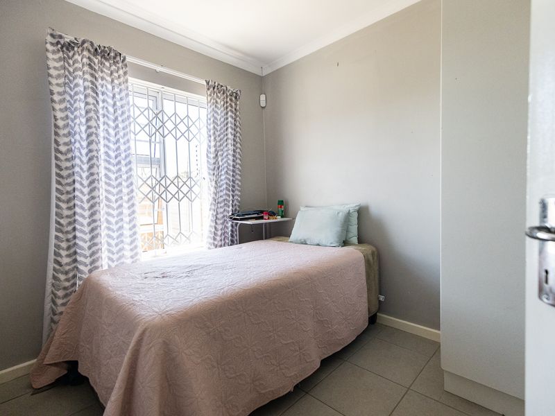 A compact bedroom featuring tiled flooring, a built-in wardrobe, and a window fitted with a security gate.
