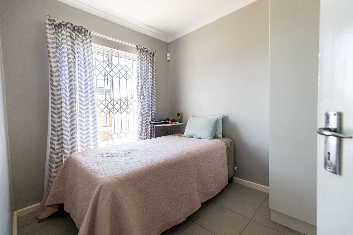 A compact bedroom featuring tiled flooring, a built-in wardrobe, and a window fitted with a security gate.