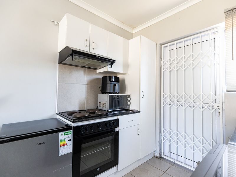 Compact kitchen featuring white cabinetry, granite countertops, built-in oven and stove, and a secure exterior door with a security gate.