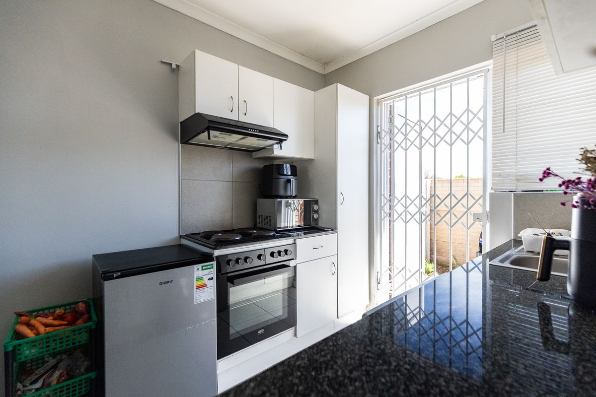 Compact kitchen featuring white cabinetry, granite countertops, built-in oven and hob, and direct access to the exterior through a security gate.