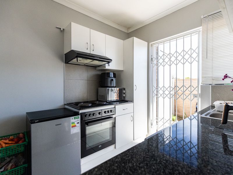 Compact kitchen featuring white cabinetry, granite countertops, built-in oven and hob, and direct access to the exterior through a security gate.