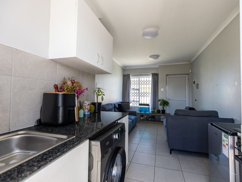 Open-plan living area featuring a compact kitchen with granite countertops, built-in cabinetry, and tiled flooring, leading to a lounge space with security gate access.