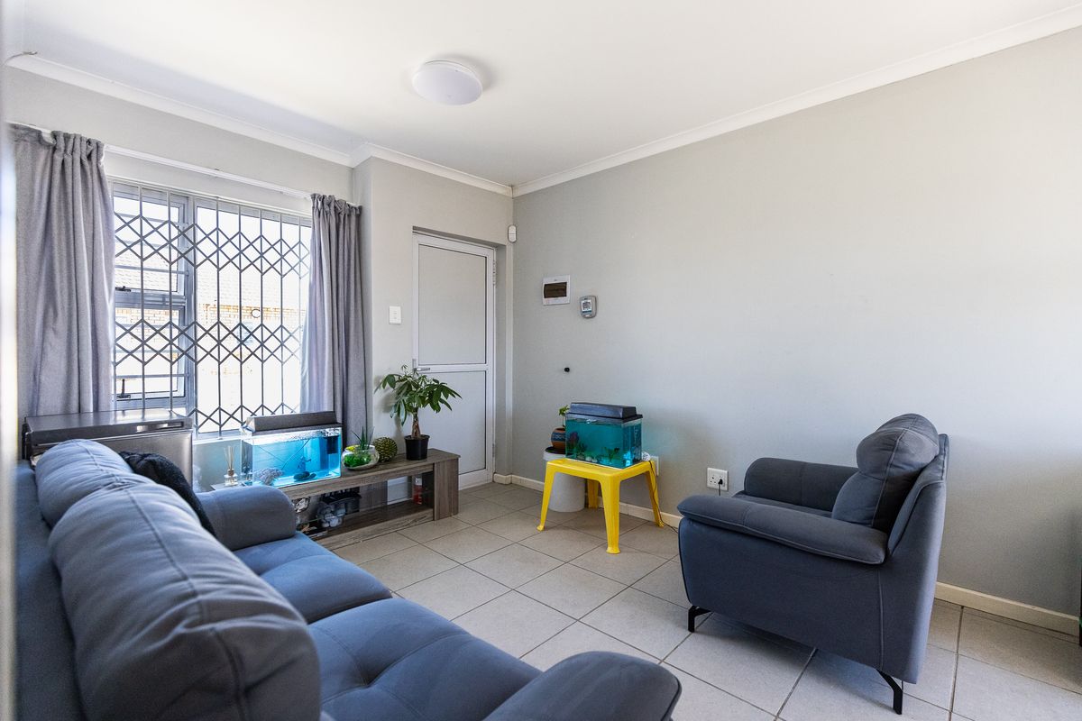 A living room featuring tiled flooring, a window with security bars, and a door leading to the exterior.