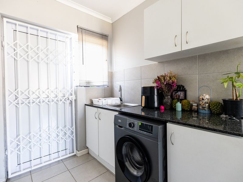A functional laundry area featuring built-in cabinetry, granite countertops, a stainless steel sink, and a secure exterior door with a security gate.