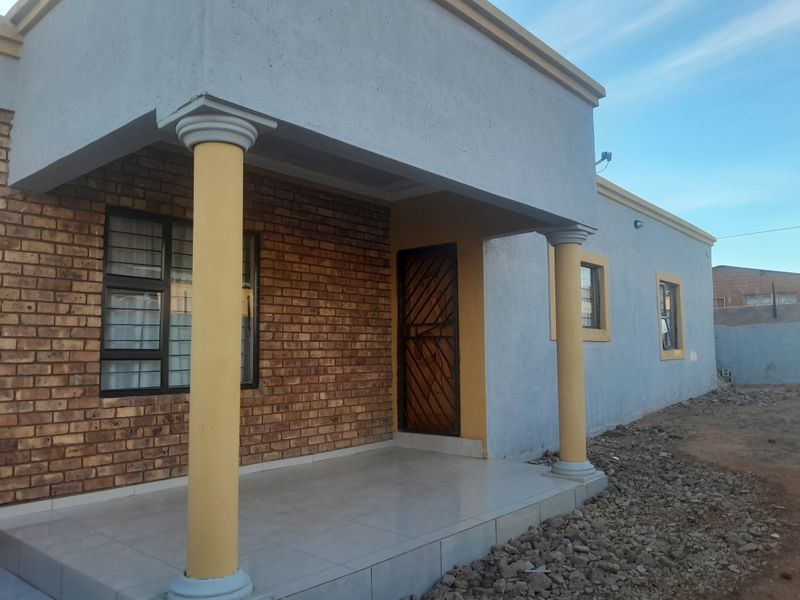 Front elevation of a house featuring a covered porch with decorative columns, face brick accents, and secure window bars.