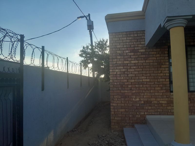 Side view of the property featuring face brick exterior, a concrete support column, and perimeter security fencing with razor wire.