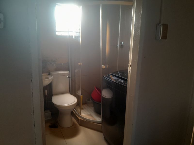 A compact bathroom featuring a shower enclosure, toilet, and wall-mounted basin, currently showing signs of wear and requiring maintenance to the wall finishes.