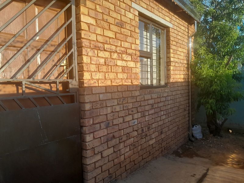 A side view of the property featuring face brick exterior walls, a timber door with a security gate, and window security bars.