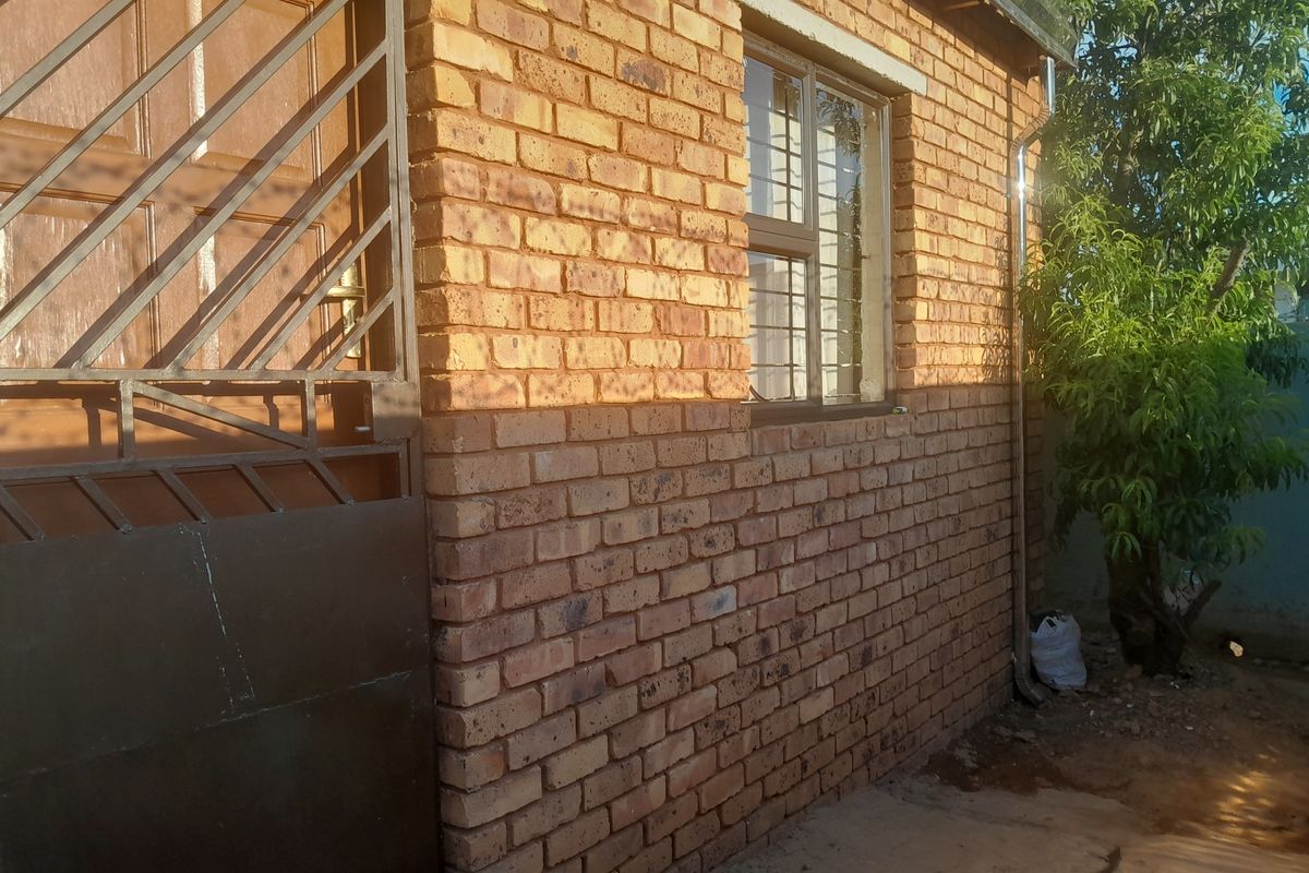 A side view of the property featuring face brick exterior walls, a timber door with a security gate, and window security bars.